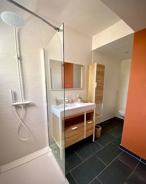 Salle de bain avec douche à l'italienne et mur terracotta.