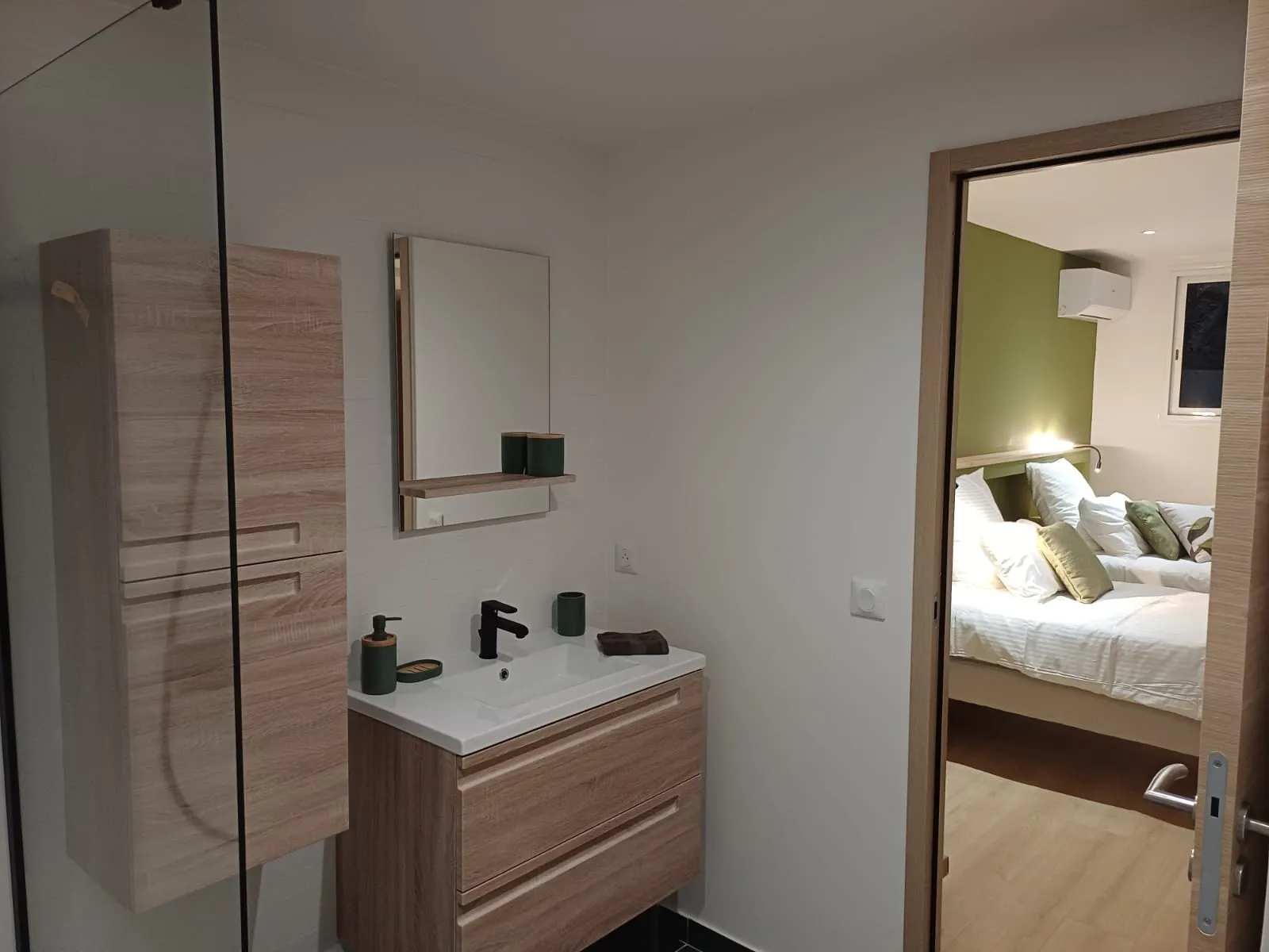 Salle de bain en bois clair ouverte sur une chambre vert kaki.
