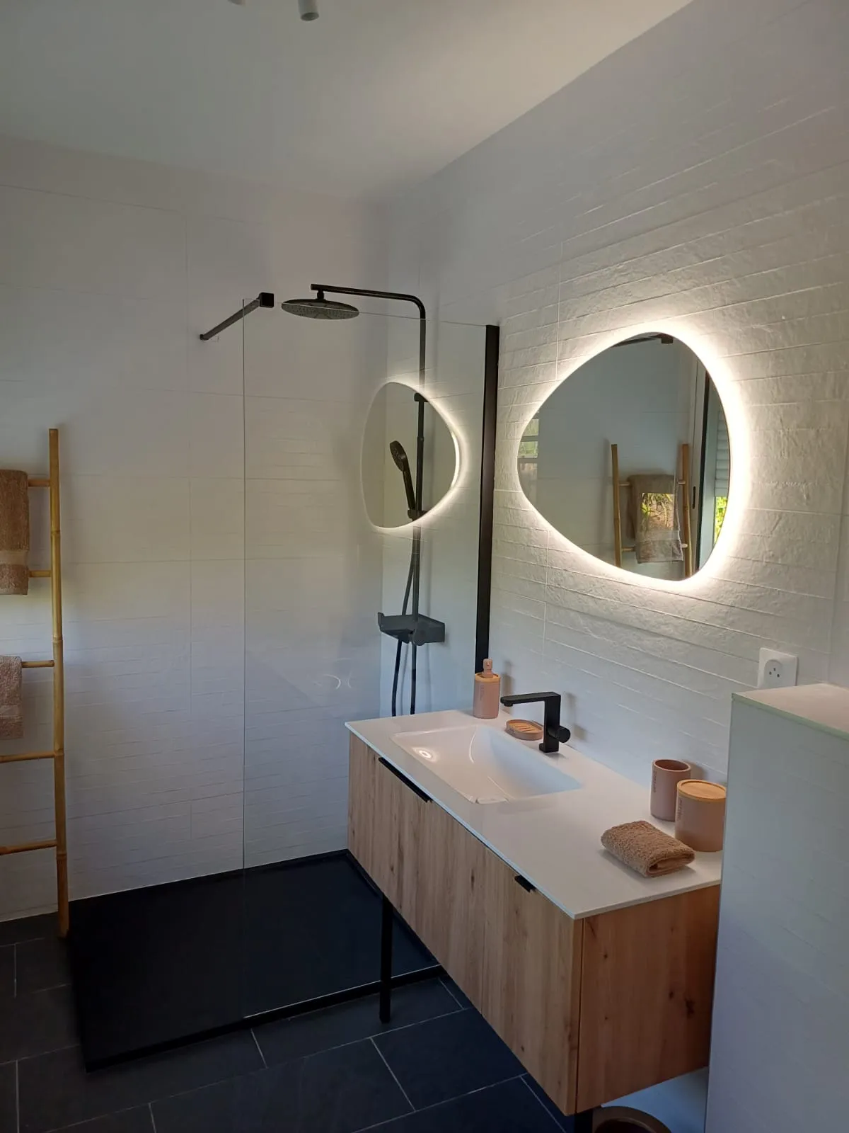 Salle de bain lumineuse, douche à l'italienne et miroir rond rétroéclairé.